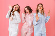 Portrait of three beautiful young girls 20s wearing colorful striped pyjamas having fun during sleepover, isolated over pink background