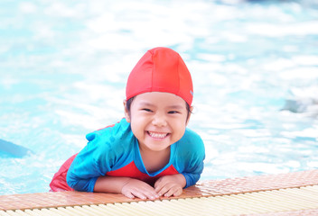 Asian children cute or kid girl wear swimming suit on swimming pool and smile with happy fun in water park for learning or refreshing and relax with exercise on summer holiday with space