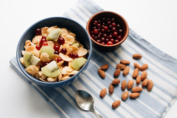 Delicious crispy cornflakes with kiwi pieces and cranberries in bowl, almonds on dish cloth, closeup, healthy breakfast