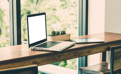 Poster - Blank screen laptop computer and tablet on wood stool table near window at cafe restaurant.mock up for display internet technology lifestyle.leisure activity.