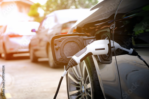Fotomural Charging modern electric car battery on the street which are the future of the Automobile, Close up of power supply plugged into an electric car being charged for hybrid