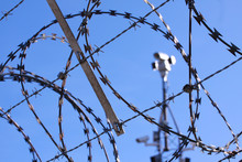 Barbed Wire Fence And Surveillance Cameras Provide Security - Blue Sky Background With Copy Space