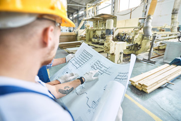 Wall Mural - Side view of two workmen discussing project plans  in workshop of modern  industrial factory, copy space