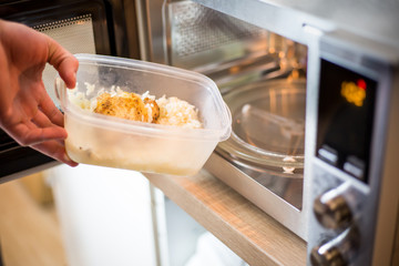 Young man hands giving the food into the microwave for warm up