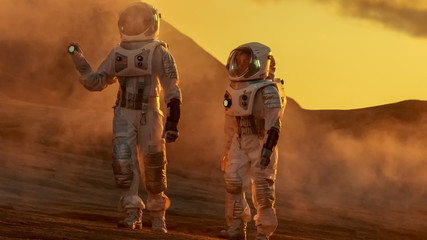 two astronauts wearing space suits walk exploring mars/ red planet. space travel and solar system co