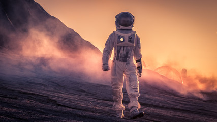Wall Mural - astronaut wearing space suit walks on the red planet/venus during sunset. in the background his base