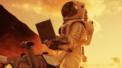 Wall Mural - astronaut in the space suit works on laptop, adjusting rover on a new alien red planet, presumably m