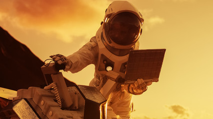 Wall Mural - astronaut in the space suit works on laptop, adjusting rover on a new alien red planet, presumably m