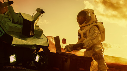 Wall Mural - astronaut in the space suit works on laptop, adjusting rover on a new alien red planet, presumably m