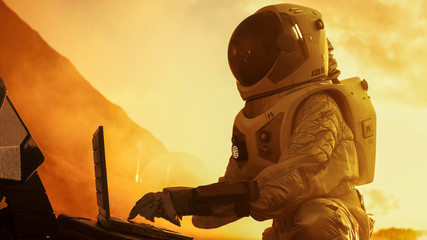 Wall Mural - astronaut in the space suit works on laptop, adjusting rover on a new alien red planet, presumably m