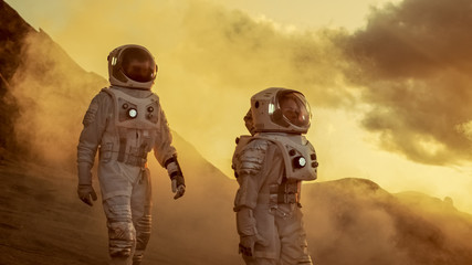 Two Astronauts in Space Suits Confidently Walking on Mars, Exploration Expedition on the Planet's Surface. Red Planet Covered in Rocks, Gas and Smoke. Humans Overcoming Difficulties.