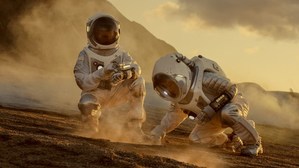 Wall Mural - two astronauts collect soils samples on alien planet, analyzing them with hands computer. mars/ red 