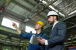 © Seventyfour - Side view portrait of two engineers discussing production in factory workshop, focus on businessman wearing hardhat and holding clipboard, copy space