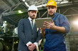 © Seventyfour - Portrait of young factory worker using digital tablet showing something to businessman wearing hardhat in workshop of modern plant, copy space