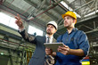 © Seventyfour - Waist up portrait of handsome businessman pointing up while discussing something with factory worker holding digital tablet, copy space