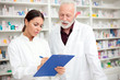 © Ivan - Medicine, pharmaceutics, health care and people concept - Serious young female and senior male pharmacists writing to a clipboard.
