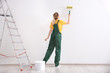 Young female decorator painting wall in empty room