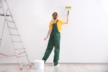 Wall Mural - Young female decorator painting wall in empty room