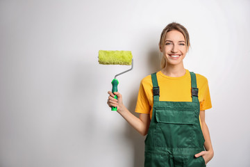 Poster - Young female decorator with paint roller on white background