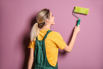 Poster - Young female decorator with paint roller near color wall