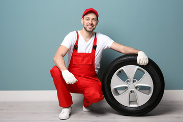 Wall Mural - Male mechanic in uniform with car tire on color wall background