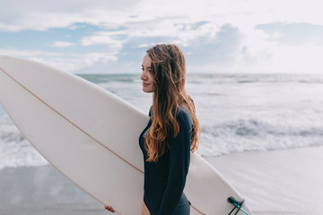 Portrait of young beautiful girl with long light-brown hair going on the surf lesson with surf board, sport lifestyle, active stylish girl