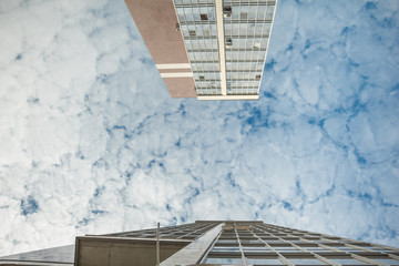 a perspective on the upper parts of tall buildings made of steel and glass on the blue cloudy sky background