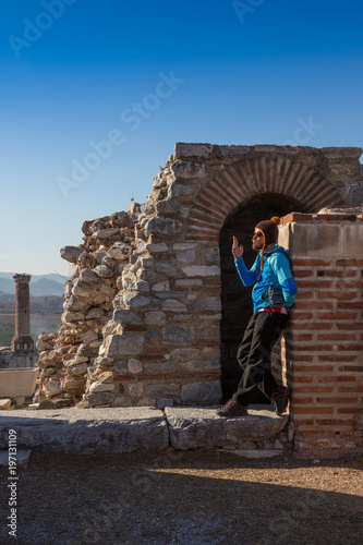 Fotografia, Obraz Man in baseball cap NYC is sitting under the arc of The Gate of Augustus in Ephesus was built to honor the Emperor Augustus and his family