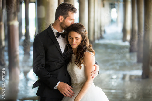 Beautiful romantic portrait of newlywed couple by water underneath gorgeous ocea Canvas-taulu