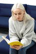 Czytanie książki. Piękna blondynka czyta książkę siedząc w domu