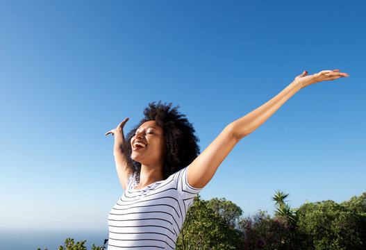 young african woman standing outdoors with arms raised and laughing