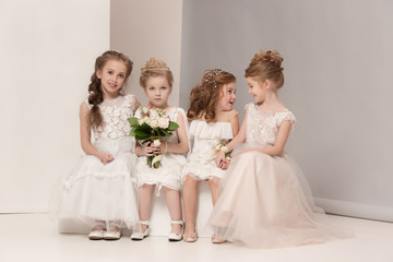 Little pretty girls with flowers dressed in wedding dresses