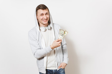 Young handsome smiling man student in t-shirt, blue jeans and light sweatshirt with hood with headphones holds two one-dollar bills and rejoiced isolated on white background. Concept of emotions