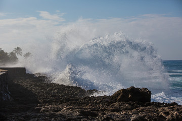 Wall Mural - tropical beach break, ocean wave crushing stone coastline, water splashes