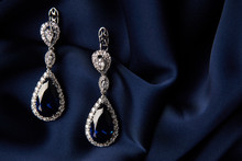 Pair of platinum earring with sapphire on blue satin background. Luxury female jewelry, close-up