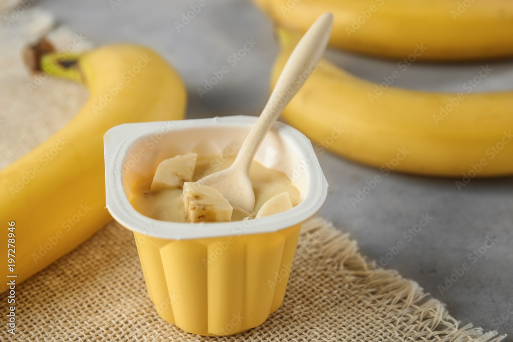 Plastic cup with yummy banana yogurt on table