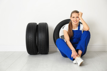 Poster - Female mechanic with car tires on light wall background