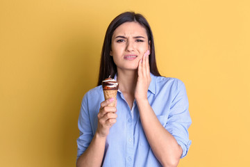 Wall Mural - Young woman with sensitive teeth and cold ice cream on color background