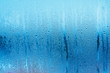Blue background of natural water condensation, window glass with high air strong humidity, large drops drip. Collecting and streaming down