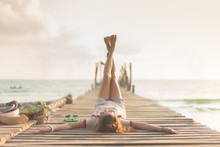 Happy Young Asian Woman Is Lift And Cross Her Leg On Wooden Bridge Pier Near The Beach During Sunset Background. - Vintage Style And Lifestyle For Travel Concept.