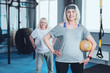 © Viacheslav Yakobchuk - Sport is waiting for you. Selective focus on a cheerful lady standing with her hand on a hip and holding a training ball while taking a group exercise class at a gym.