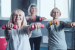 © Viacheslav Yakobchuk - Ensuring a long life. Selective focus on a lovely lady standing with her hands outstretched and beaming while doing weight lifting exercises in a gym.