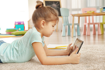 Canvas Print - Cute little girl using tablet PC while doing homework indoors