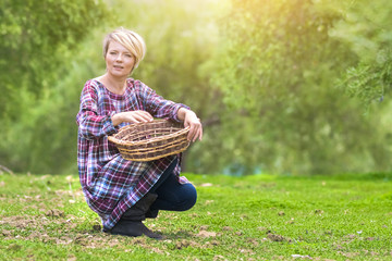 Wall Mural - Beautiful young blonde woman in a checkered dress sits with a wicker basket in the summer garden