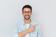 © Z A C - Cheerful young smiling bearded male model wearing trendy glasses, points away, demonstrates something at blank copy space for your advertisment or text in studio. People and lifestyle concept.