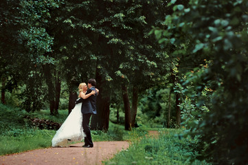 Bride and groom at wedding Day walking Outdoors on summer nature. Bridal couple, Happy Newlywed woman and man embracing in green park. Loving wedding couple outdoor. Bride and groom in honeymoon