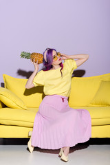 Wall Mural - beautiful young woman on yellow couch holding pineapple near head