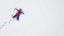 Child Girl Playing And Making A Snow Angel In The Snow. Top Flat Overhead View