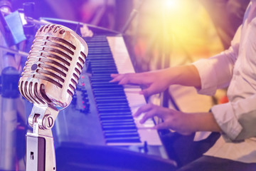 Close up retro microphone with musician playing keyboard synthesizer on band in night concert background