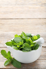 Wall Mural - Fresh mint leafs in mortar on grey wooden table